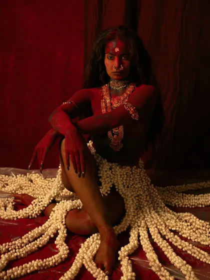 A full-body conceptual shot exploring the theme of creation and destruction. The use of red body paint and jasmine flowers creates a stark, visually arresting contrast.