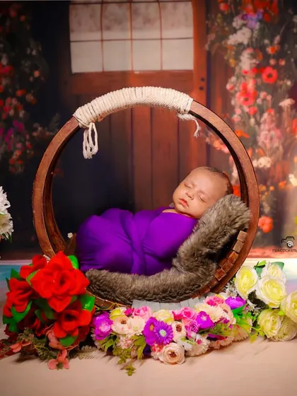 A beautifully staged newborn photo. The baby sleeps in a round hanging prop, surrounded by a vibrant floral arrangement in our studio.