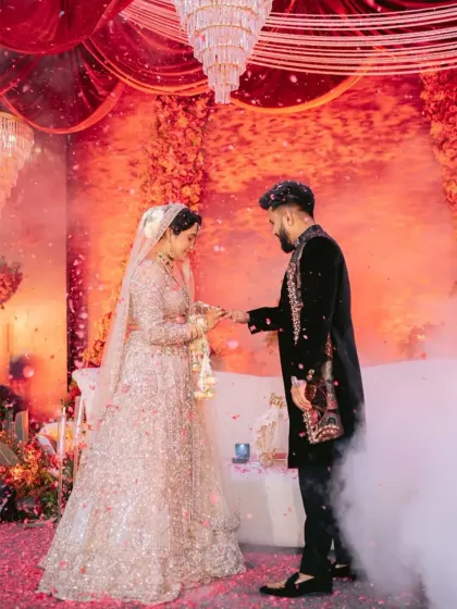 During the ring ceremony, the groom's dark, modern sherwani stands out against the romantic, floral backdrop. The rich velvet and detailed embroidery on his outfit create a look of sophisticated celebration.