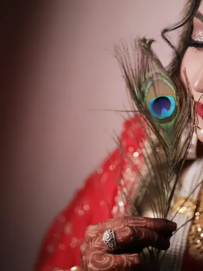 A creative and artistic bridal portrait using a peacock feather as a prop. This close-up shot highlights the bride's flawless makeup and serene expression.