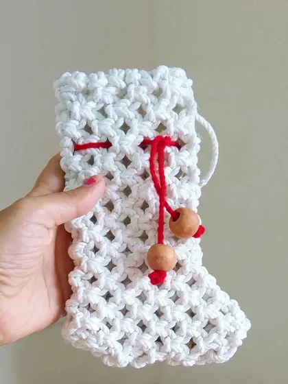 A handmade macrame Christmas stocking, ready to be filled with small gifts and treats. The red drawstring adds a festive touch.