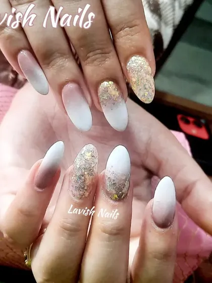 A unique ombré effect blending from a nude base to a white tip, with accent nails featuring a chunky gold glitter fade.