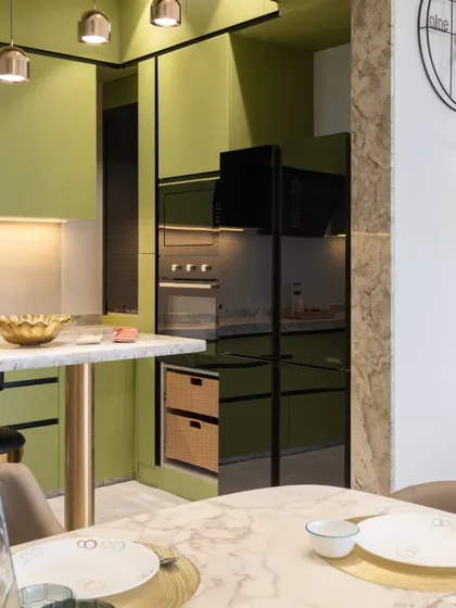 Detail of the integrated appliance unit in the Kalyan kitchen. The black glass of the oven and microwave is framed perfectly by the sage green cabinetry, creating a sleek, modern focal point.