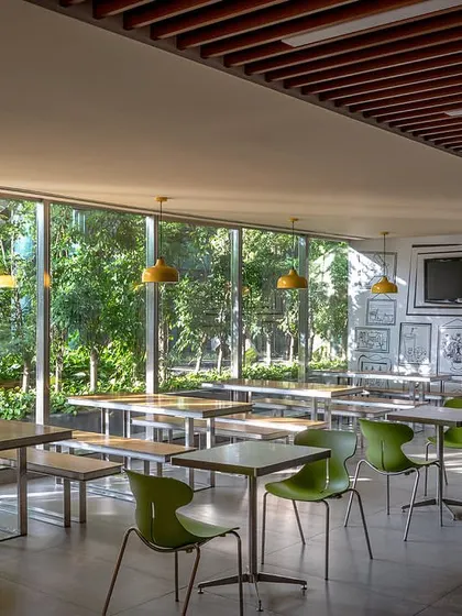 The ground-floor cafeteria is designed with large glass windows overlooking the lush landscape, creating a bright and refreshing space for employees with industrial-style furniture and lighting.