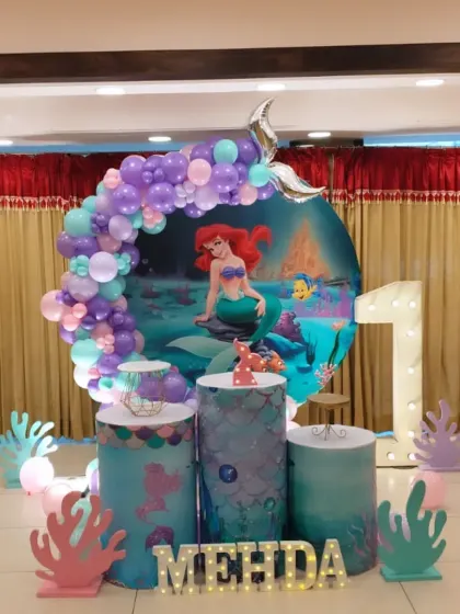 We went under the sea for Medha's first birthday with this mermaid theme. The setup features a round backdrop with Ariel, an ocean-toned balloon garland, and coral-shaped cutouts to complete the underwater look.
