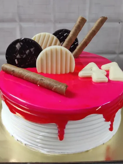 A 41st birthday cake with a bright pink glaze and drip effect. It's topped with chocolate wafer rolls and white chocolate decorations.