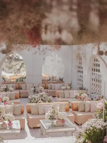 A view from within a guest lounge area, looking out onto the main ceremony space. The design uses layers of jali screens and floral arrangements to create depth and visual interest.