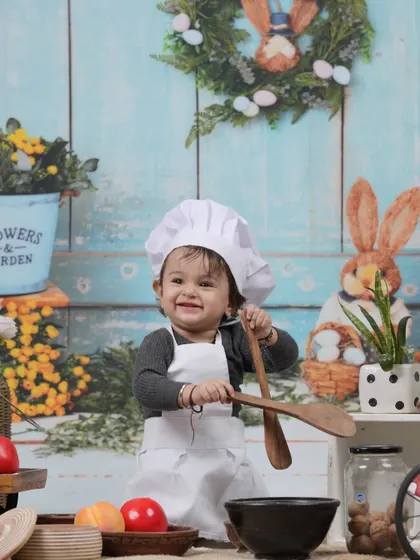 Our little chef is ready to cook up some smiles. This adorable milestone session features a baby girl in a chef's hat and apron, playing with wooden spoons and bowls.