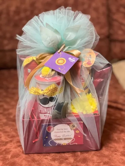 The fully wrapped version of the snack-filled Rakhi hamper, presented in light blue tulle with a gold ribbon and festive tag.