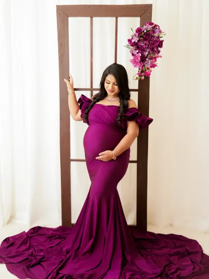 A regal and elegant portrait. The mom-to-be looks stunning in a deep purple gown, standing gracefully against a simple backdrop.