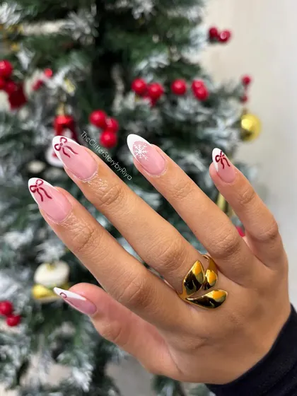 A delicate and festive French manicure for the holidays. This design includes white tips, hand-painted red bows, and a subtle snowflake accent.