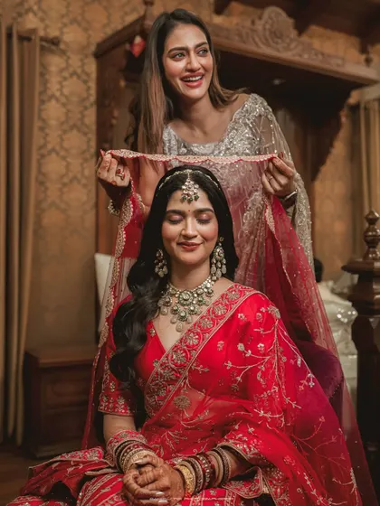 A candid moment of a bridesmaid adjusting the bride's veil. The bride's serene expression and the gentle care of her friend make this a beautiful shot.