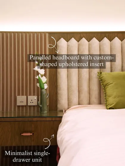 A paneled headboard with a custom-shaped upholstered insert creates a unique focal point in this bedroom. The minimalist single-drawer side unit maintains a clean and modern aesthetic.