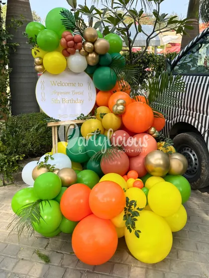 A vibrant balloon arrangement welcomes guests to Aryaveer's 5th birthday, with a custom sign and colors that pop against the jungle-themed jeep.