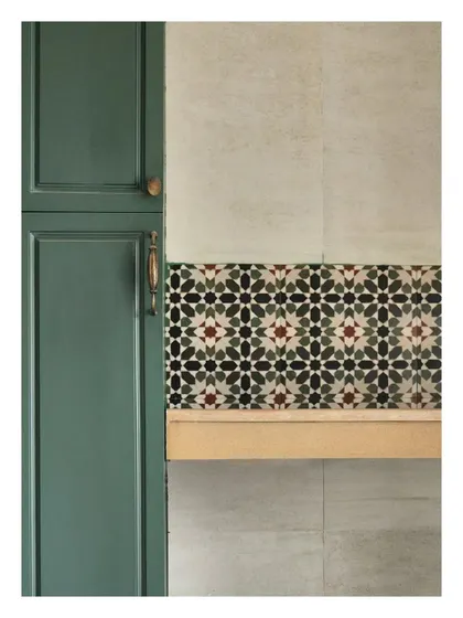 A beautiful juxtaposition of materials in a kitchen. The deep green of the shaker-style cabinet contrasts with the intricate pattern of the Moroccan-style tiles and the simple wooden shelf.