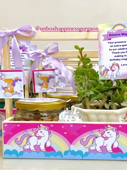 A magical unicorn-themed return gift for a third birthday. This basket combines a jade plant with jars of treats, all decorated in a whimsical pink and lavender palette.