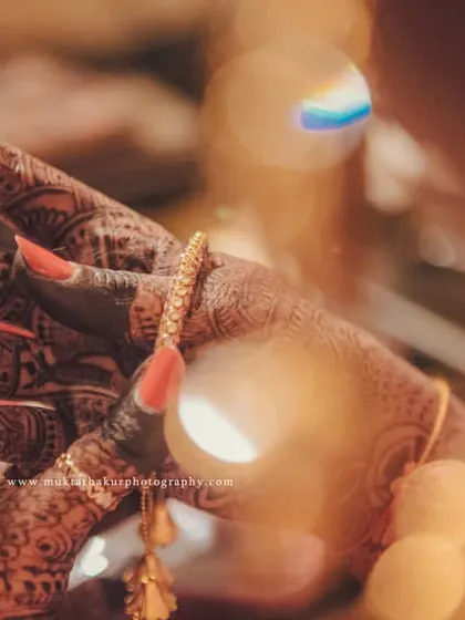 An artistic shot of the bride's hands, adorned with dark mehendi and beautiful jewelry, with a dreamy bokeh effect.