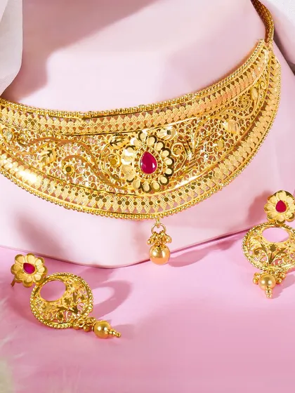 A stunning close up of a gold choker necklace set with a ruby. The piece is displayed on a pink bust, which mimics how it would be worn and highlights its intricate details against a soft background.