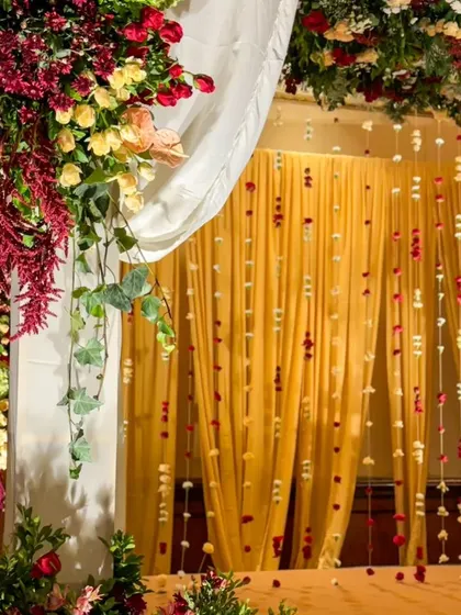 The backdrop of the mandap features a curtain of delicate, individually strung roses against a warm yellow drape, adding texture and detail.