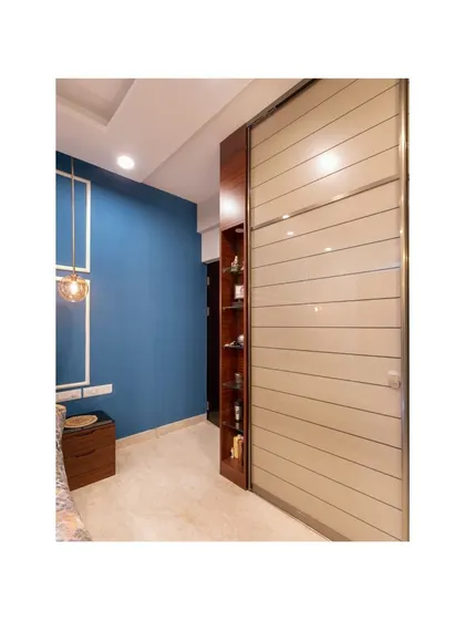 A sleek sliding wardrobe with alternating frosted glass and wood-finish panels defines this bedroom, complemented by a bold blue accent wall for a touch of modern sophistication.