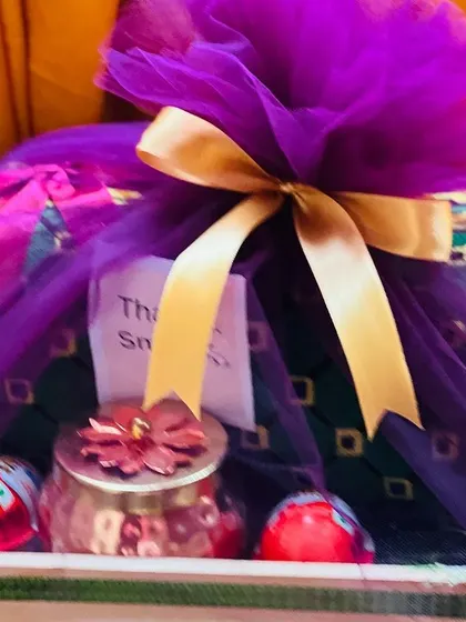 The same gift hamper, now wrapped in vibrant purple net with a gold ribbon. The wrapping completely transforms the gift, making it perfect for a festive occasion.