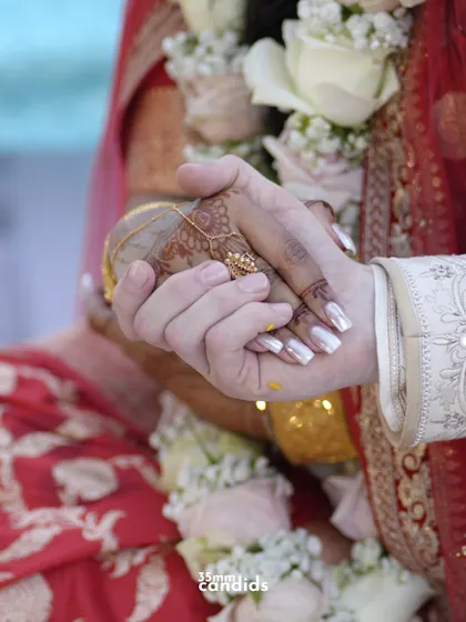 A tender moment showing the groom holding the bride's hand, her mehendi and his watch telling a story of two different worlds coming together.