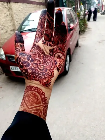 A candid shot of a beautiful henna stain. This shows the back of the hand, where the design features a lovely mandala and detailed finger work, all in a rich mahogany color.