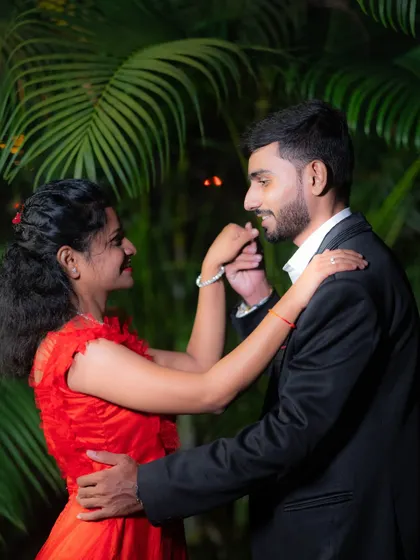 A romantic evening pre-wedding shot where the groom-to-be gently kisses his partner's hand amidst lush green foliage.