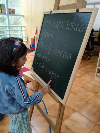Reading the recipe from the board is the first step in our baking lesson. This integrates practical life with literacy, showing children how reading is a useful tool in everyday activities.