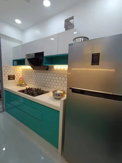 This wider view shows the efficient layout of the teal kitchen, with the refrigerator placed conveniently at the end of the counter. The glossy finish on the cabinets reflects light, making the space feel bigger and brighter.