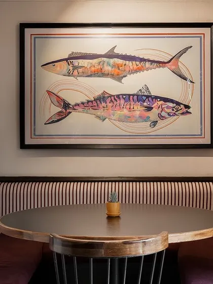 A cozy dining nook at Klaa Kitchen, featuring custom artwork of fish and striped upholstery. This intimate corner is perfect for small groups, offering a comfortable and thoughtfully designed space.