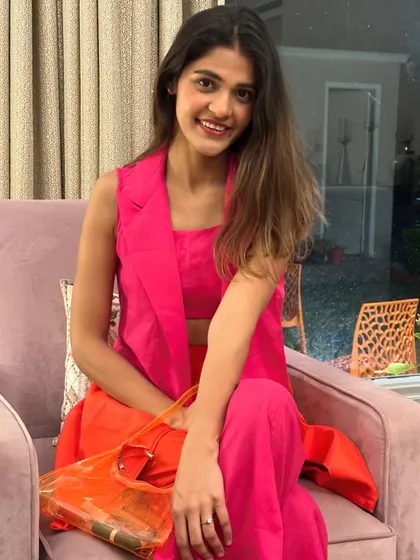 A seated portrait showing the bright colors of my Holi co-ord set. The transparent orange bag is a fun and trendy accessory that complements the outfit.