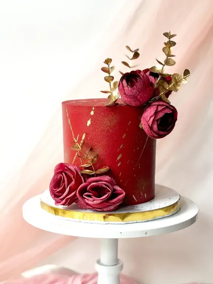 A bold and dramatic red cake with gold splatter. It's elegantly topped with deep red roses and gilded eucalyptus leaves for a luxurious feel.