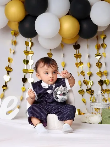 A closer look at the stylish first birthday setup, showing the little boy interacting with a disco ball prop. The gold heart streamers add a touch of glamour to the scene.