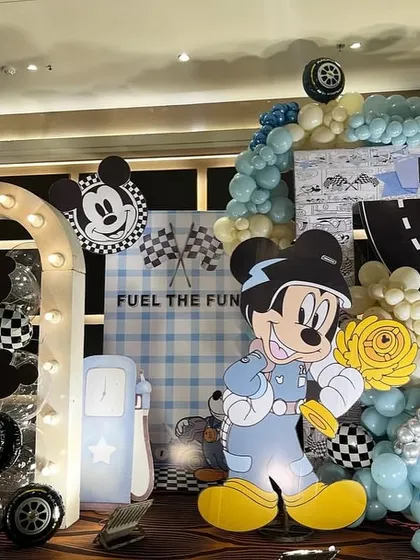 A close-up of the Mickey Mouse racing theme, showing the 'Fuel the Fun' sign, a gas pump prop, and a lighted arch.