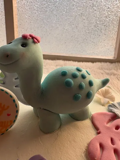 A close-up of the adorable, hand-sculpted dinosaur topper. I added a little flower to her hair for a sweet, personal touch.
