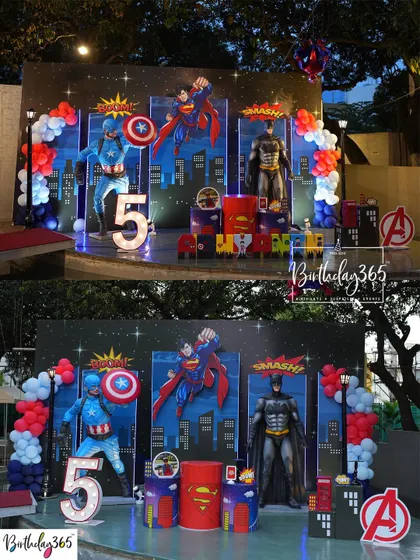 A full stage setup for a 5th birthday, featuring life-sized statues of Captain America, Superman, and Batman against a city skyline.