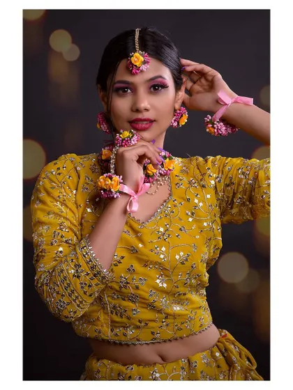 A close-up shot of a model in a festive yellow lehenga. The focus is on the intricate floral jewelry and the beautiful makeup.