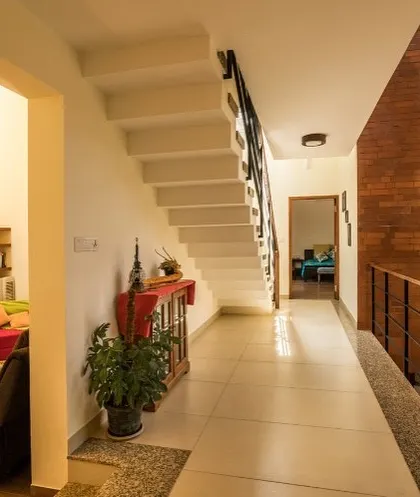 An exposed brick accent wall brings texture and warmth to this hallway in the Reshma Residence. It contrasts with the clean white walls and serves as a backdrop for the home's central staircase, guiding movement through the space.