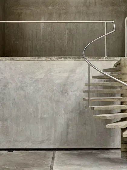 This sculptural spiral staircase, made of pre-cast concrete steps, stands as a functional art piece against a raw concrete wall in the Automobile Design Studio. It represents our commitment to integrating crafted details even in large-scale industrial projects.
