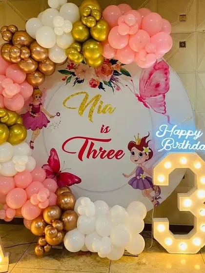 A fairy-themed 3rd birthday party. This decoration features a personalized backdrop, a pink and gold balloon arch, and marquee letters and numbers.