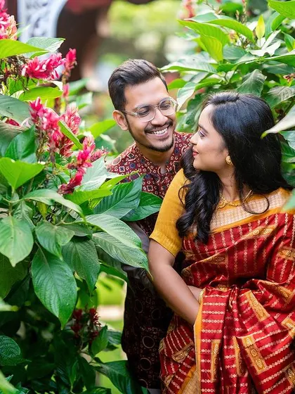 A happy, candid moment of a couple peeking through vibrant red and green foliage.