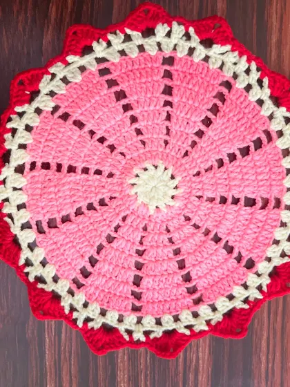 A round thalkosh with a pinwheel design in pink and off-white, framed by a bold red border.