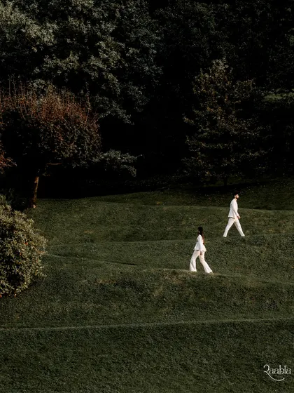 The couple dressed in white, walking in parallel across the rolling green hills of Lake Como, creating a minimalist and artistic composition.