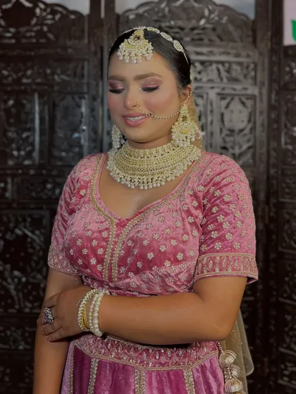A soft and romantic bridal look in a beautiful pink velvet lehenga. The makeup features a gentle pink eyeshadow, a flawless base, and pearl jewelry for an ethereal vibe.