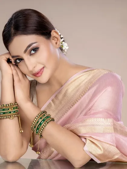 A model wearing a pink silk saree with green bangles, showcasing how traditional jewellery can be styled for a soft, elegant look in a studio setting.