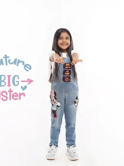 A fun and modern sibling announcement, with a 'Future Big Sister' graphic next to the smiling girl who is showing off sonogram pictures on her overalls.