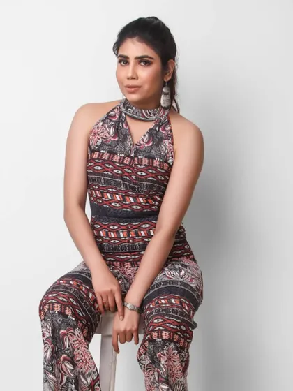 This seated portrait shows a model in a patterned halter-neck jumpsuit. The relaxed yet poised pose makes it a strong image for a commercial or lifestyle fashion portfolio.