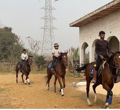 Riders in a line follow an instructor past the stables. This drill helps students learn to control their horse's speed and maintain spacing.