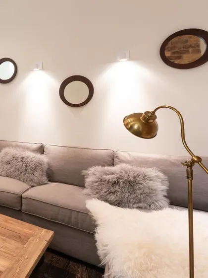 A cozy living room corner with a comfortable grey sofa, plush faux fur pillows, and warm accent lighting, creating a perfect spot for relaxation.